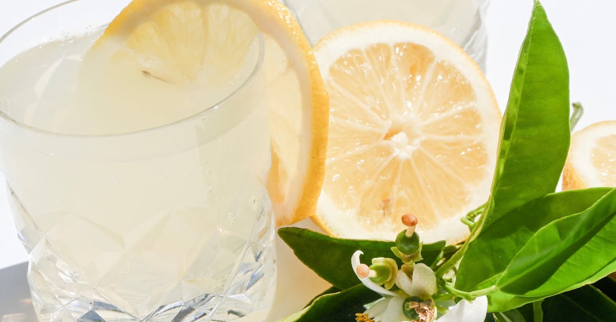 A bright still life of citrus drinks garnished with lemons and white blossoms.